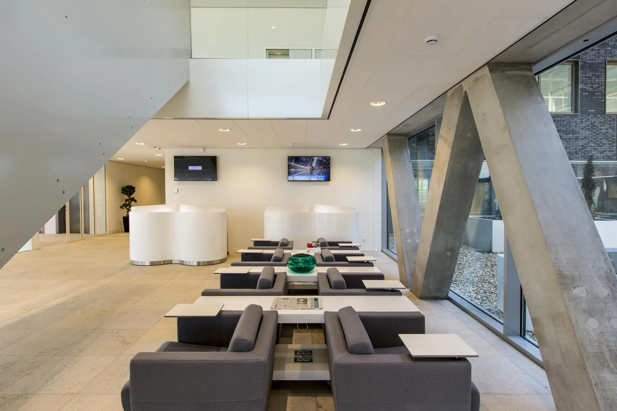 Moderne wachtruimte met grijze fauteuils, witte tafels en grote betonnen steunpilaren in een kantoorgebouw aan het Airportplein in Rotterdam.